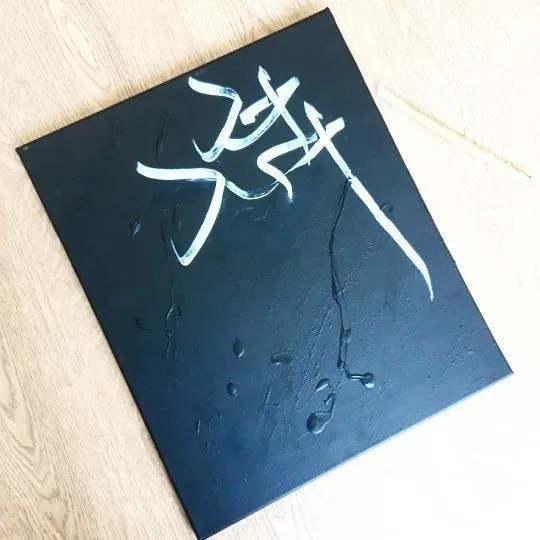Un tableau bleu nuit avec le mot Ahad calligraphié en blanc